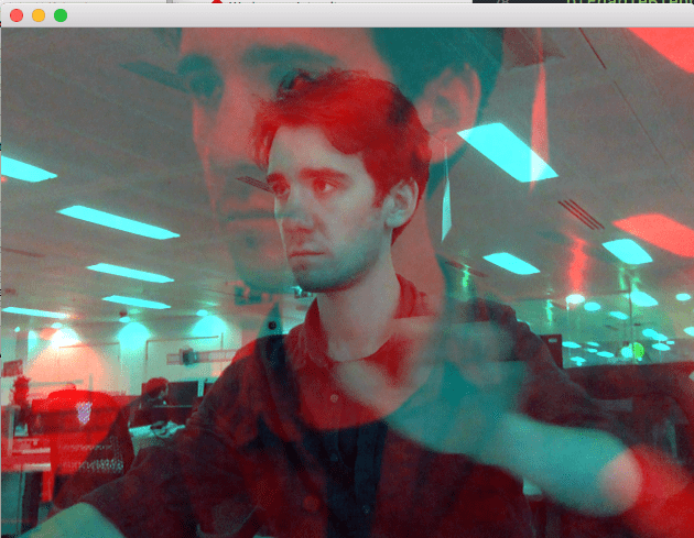 Struan appears with a blue hue in an office. A larger image with a red hue appears super imposed over the original image. Struan is waving.