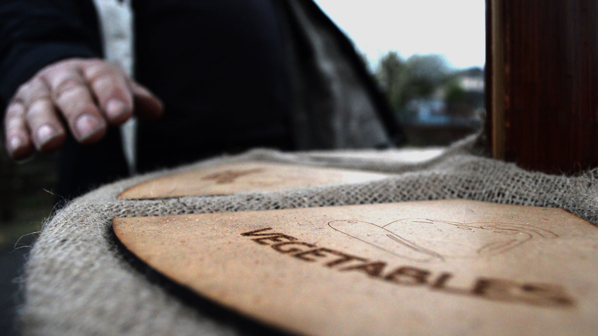 A wooden totem is shown with a series of buttons set in hessian. The buttons circulate the central column and have labels laser cut into them. The labels indicate different types of British grown foods.