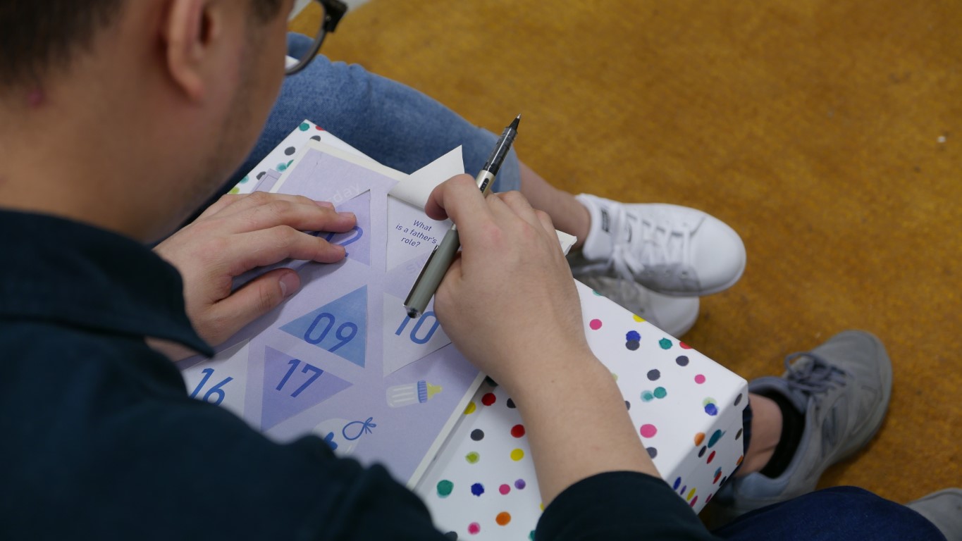 A man holds up a flap in a paper calendar revealing a question